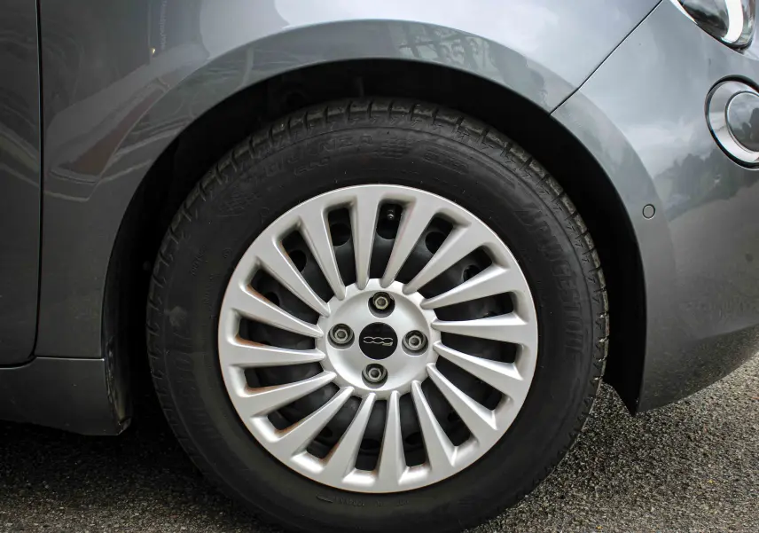 Gros plan sur la roue avant droite d'une Fiat 500 électrique gris minéral métal avec jante argentée stylisée.