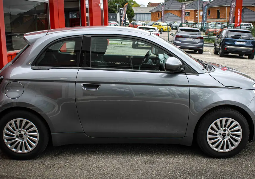 Profil côté gauche d'une Fiat 500 électrique 2023 gris minéral métal, avec jantes alliage et lignes arrondies.