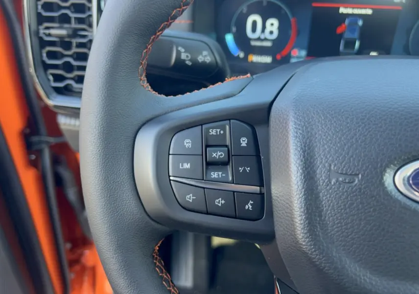 Gros plan sur le volant cuir du Ford Ranger Wildtrak orange, avec commandes multifonctions et tableau de bord numérique.
