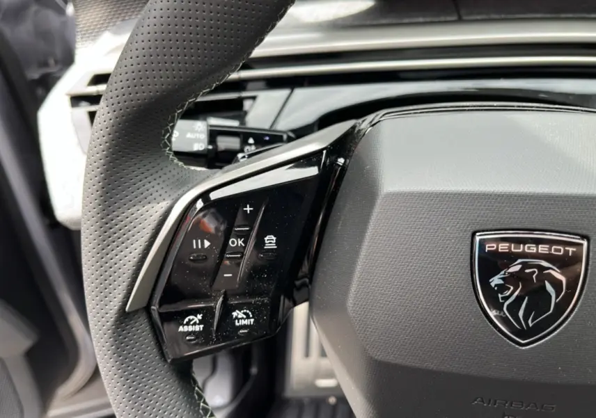 Gros plan sur le volant cuir perforé de la Peugeot 5008 Hybrid 145 GT avec commandes multifonctions et logo lion central.
