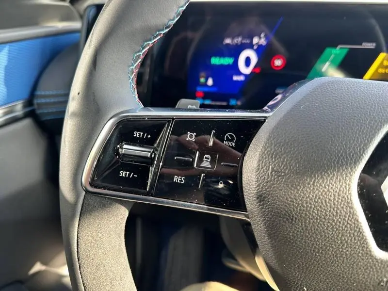 Gros plan sur les commandes au volant côté gauche du Renault Scénic E-Tech gris, avec tableau de bord numérique en arrière-plan.
