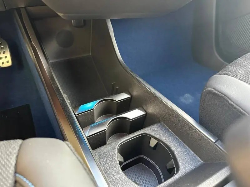 Gros plan sur les porte-gobelets avant et rangement central du Renault Scénic E-Tech gris Schiste, intérieur avec tapis bleu.