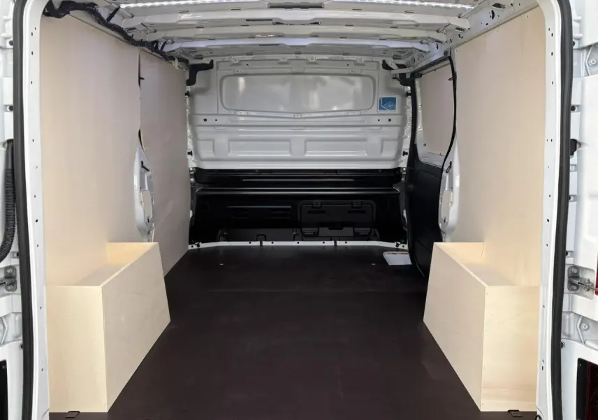 Intérieur arrière du Renault Trafic Fourgon blanc glacier, vue de la zone de chargement avec habillage bois complet.
