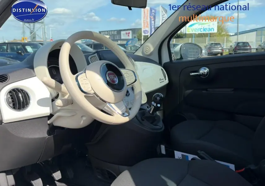 Vue intérieure côté conducteur du tableau de bord blanc et volant beige d'une Fiat 500 2023 essence avec boîte manuelle.