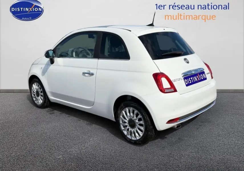 Fiat 500 blanc vue 3/4 arrière côté gauche, jantes alu et vitres teintées visibles sur fond neutre.