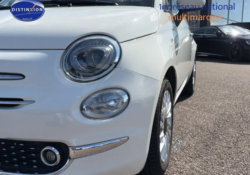 Vue 3/4 avant droit d'une Fiat 500 blanche mettant en valeur ses phares ronds et jantes alu brillantes.