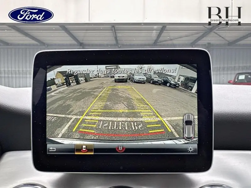 Écran de caméra de recul montrant une vue arrière large d’un parking avec plusieurs voitures garées.