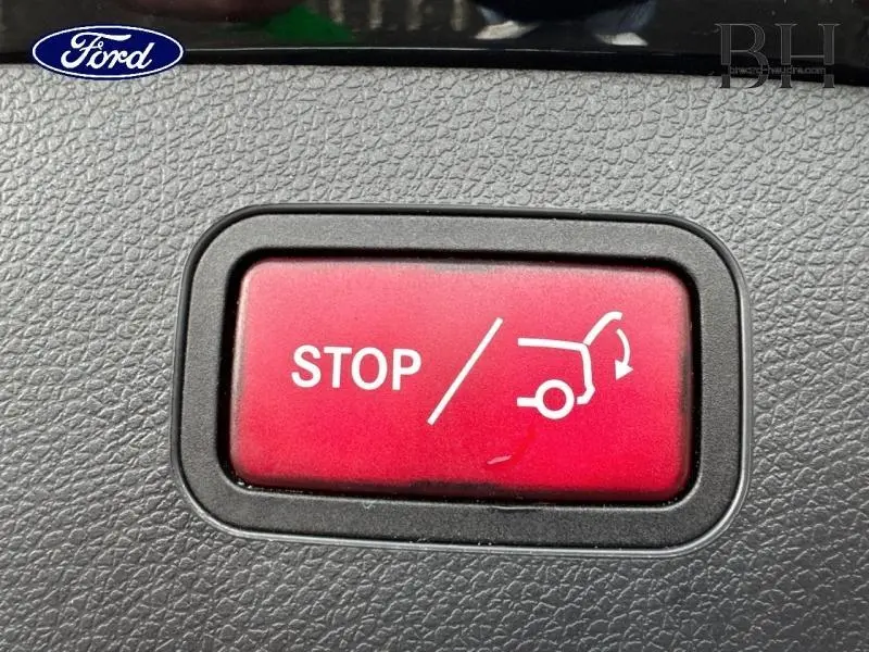 Image ne correspondant pas au véhicule décrit, montrant un bouton rouge "STOP" pour coffre électrique sur tableau de bord noir texturé.