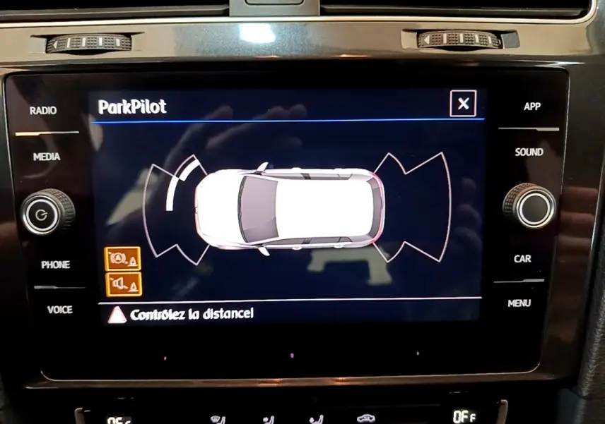 Écran tactile intérieur montrant le système ParkPilot de la Volkswagen Golf noire, vue de dessus du véhicule en blanc.