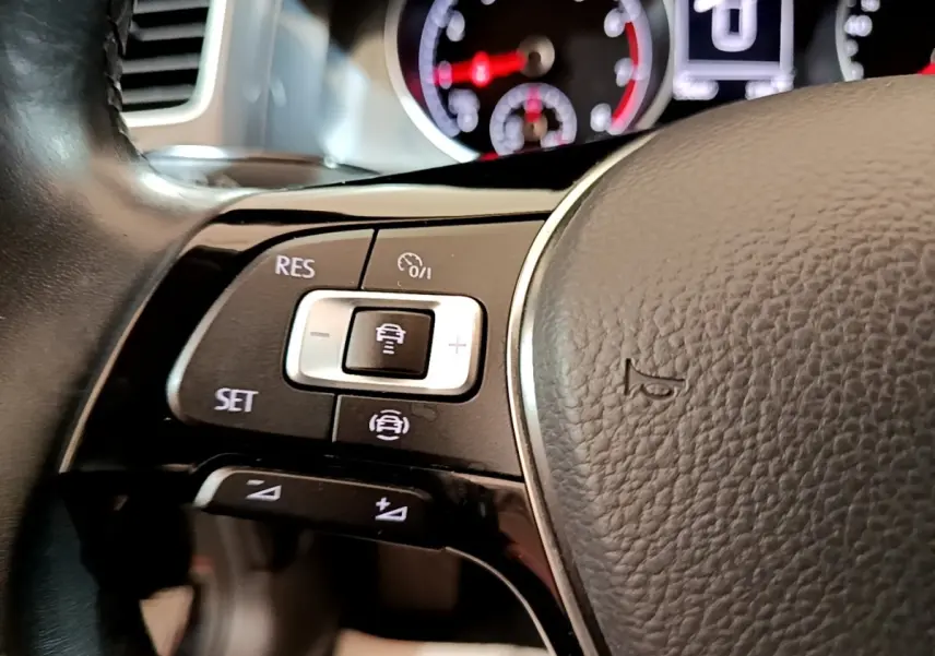 Gros plan sur le volant cuir noir de la Volkswagen Golf 2019, avec commandes multifonctions et tableau de bord flou.