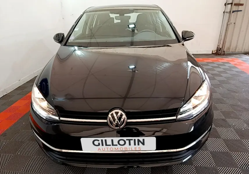 Vue avant d'une Volkswagen Golf noire 2019 avec phares allumés dans un garage fermé.