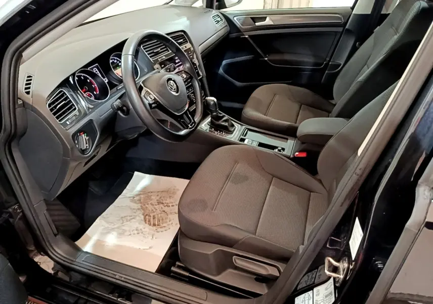 Vue intérieure côté conducteur d'une Volkswagen Golf noire avec volant cuir multifonctions et sièges tissu gris.