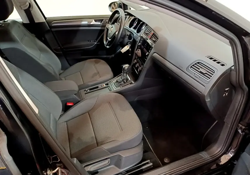 Vue intérieure côté conducteur d’une Volkswagen Golf noire de 2019 avec sièges tissu gris et volant cuir multifonctions.