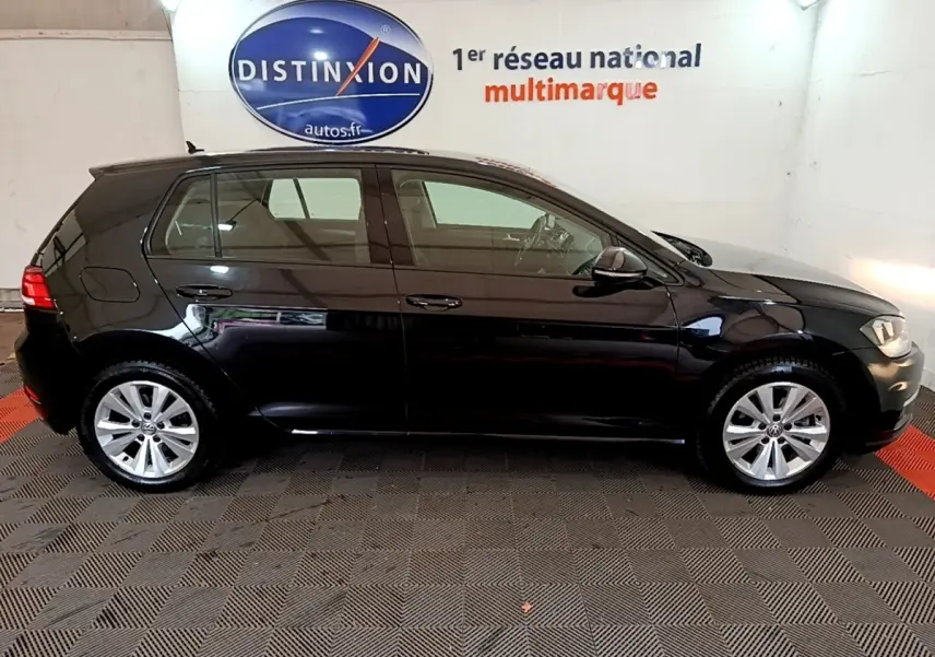 Profil droit d'une Volkswagen Golf noire 2019 stationnée en intérieur avec logo Distinxion en arrière-plan.