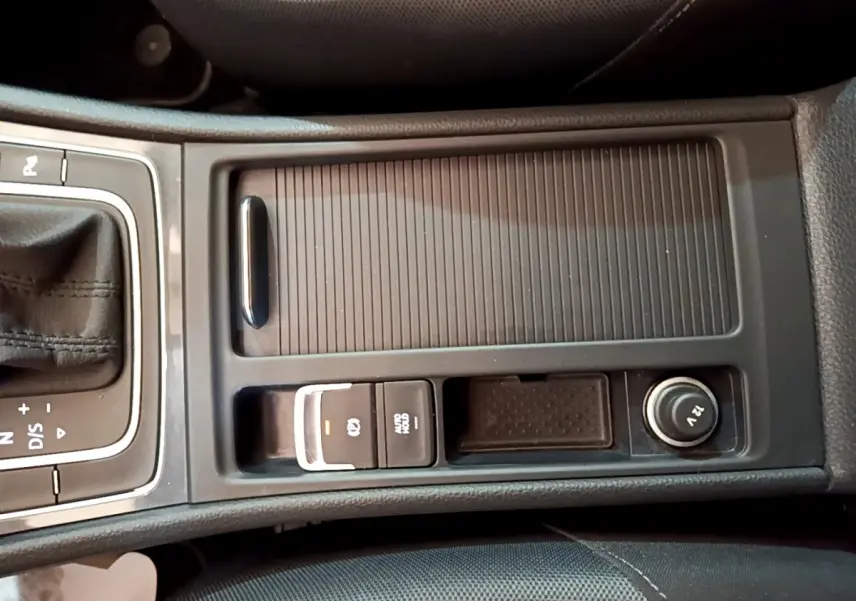 Vue rapprochée de la console centrale noire de la Volkswagen Golf 1.0 TSI 115 DSG7 avec frein à main électrique et prise 12V.