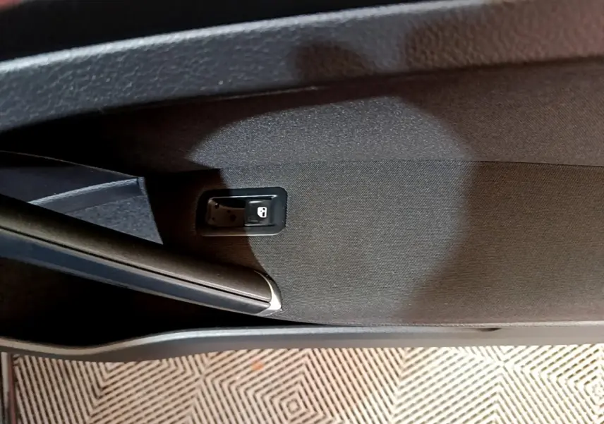 Détail de la commande d'ouverture de coffre intégrée dans le revêtement intérieur noir de la porte arrière droite d'une Volkswagen Golf noire.
