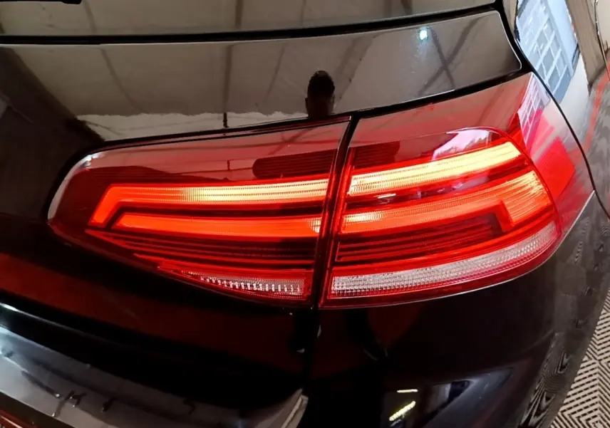 Gros plan sur le feu arrière droit allumé d’une Volkswagen Golf noire, reflétant l’environnement intérieur.