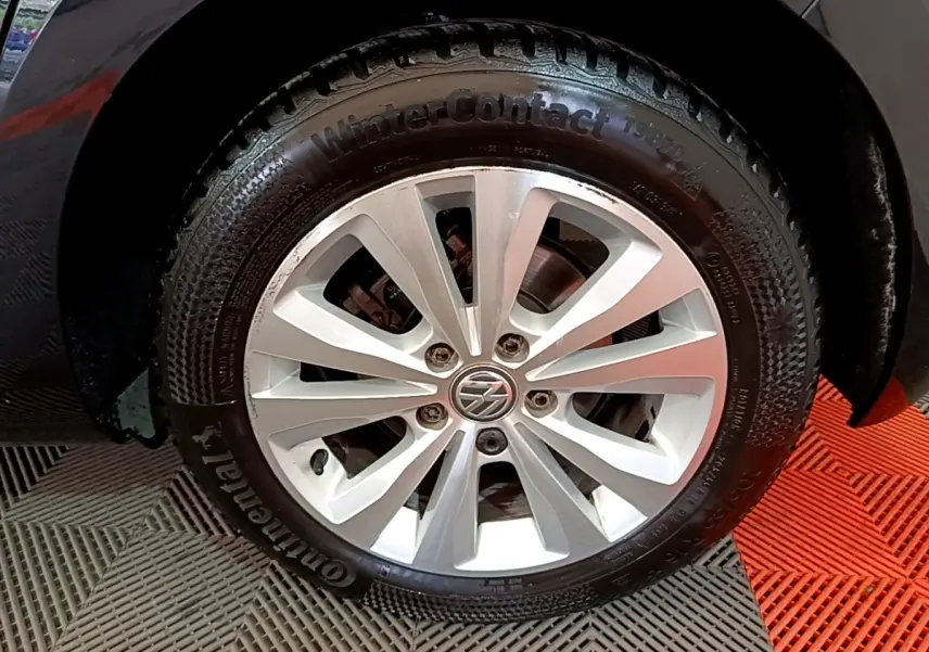 Gros plan sur la roue avant droite noire d'une Volkswagen Golf 1.0 TSI 115 DSG7 avec jante argentée et logo VW.