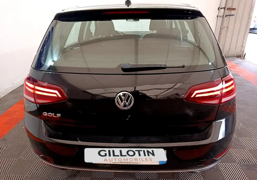 Vue arrière d'une Volkswagen Golf noire de 2019 avec feux LED allumés dans un garage.