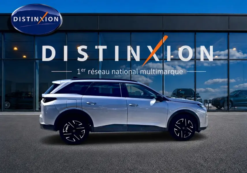 Peugeot 5008 Hybrid 145 allure gris artense en profil droit devant une vitrine Distinxion, jantes alu noires et toit noir.