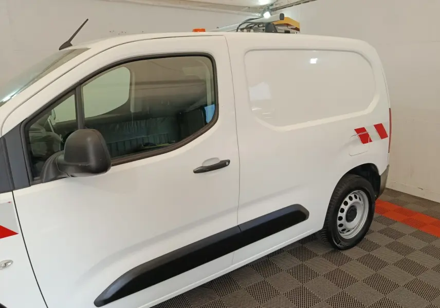 Vue de profil côté gauche d’un Citroën Berlingo blanc 2021 avec bandes rouges réfléchissantes et toit équipé d’un gyrophare.