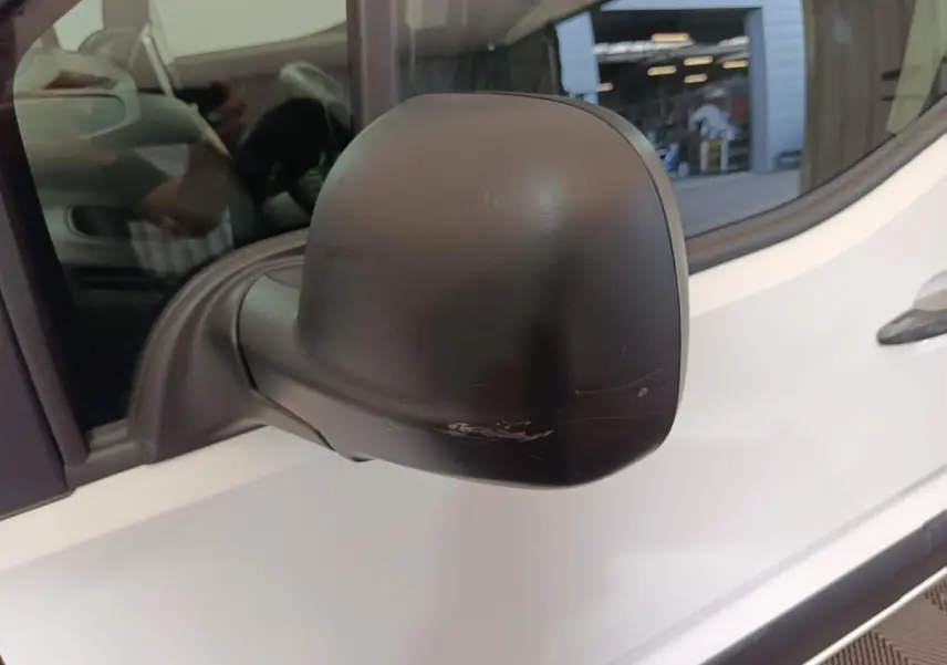 Gros plan sur le rétroviseur noir côté gauche d'un Citroën Berlingo blanc 2021 avec une rayure visible.