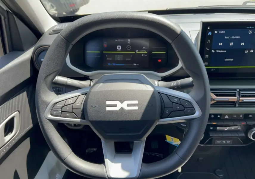 Vue frontale du volant et tableau de bord numérique du Dacia Spring électrique gris éclair avec écran tactile central.