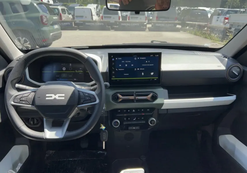 Vue intérieure frontale du tableau de bord et volant du Dacia Spring électrique gris éclair avec écran tactile et commandes au volant.