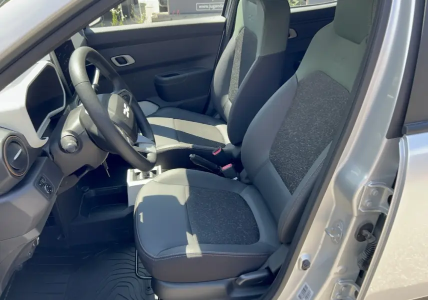 Vue intérieure côté conducteur de la Dacia Spring électrique gris éclair, avec sièges bi-matière cuir tissu et volant noir.