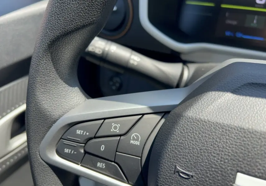 Gros plan sur les commandes au volant du Dacia Spring électrique 65 Extreme, avec tableau de bord numérique en arrière-plan.