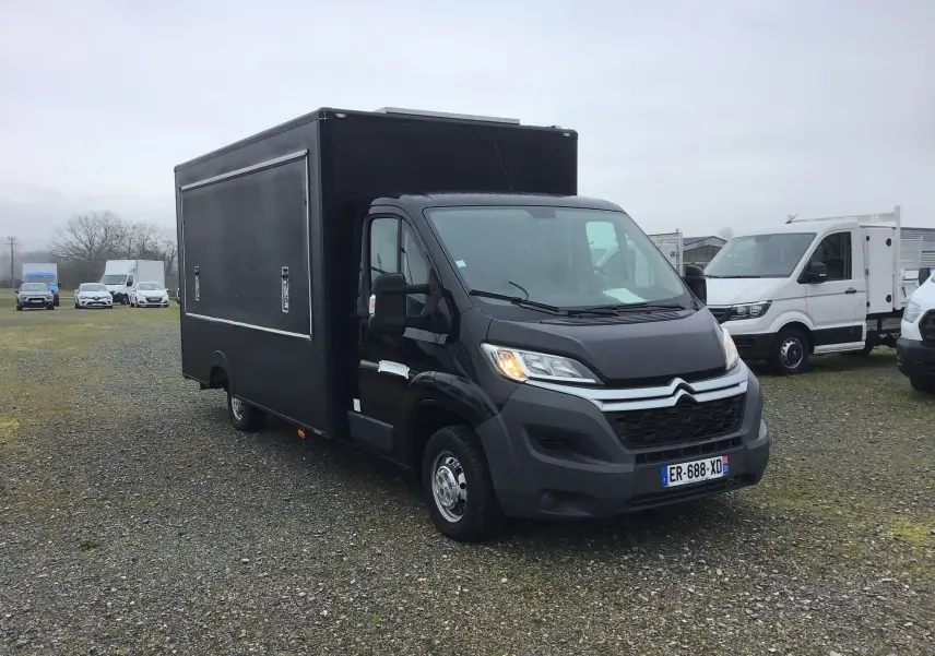 Vue 3/4 avant d'un Citroën Jumper plancher cabine gris graphito avec caisse magasin food truck noire sur un parking.