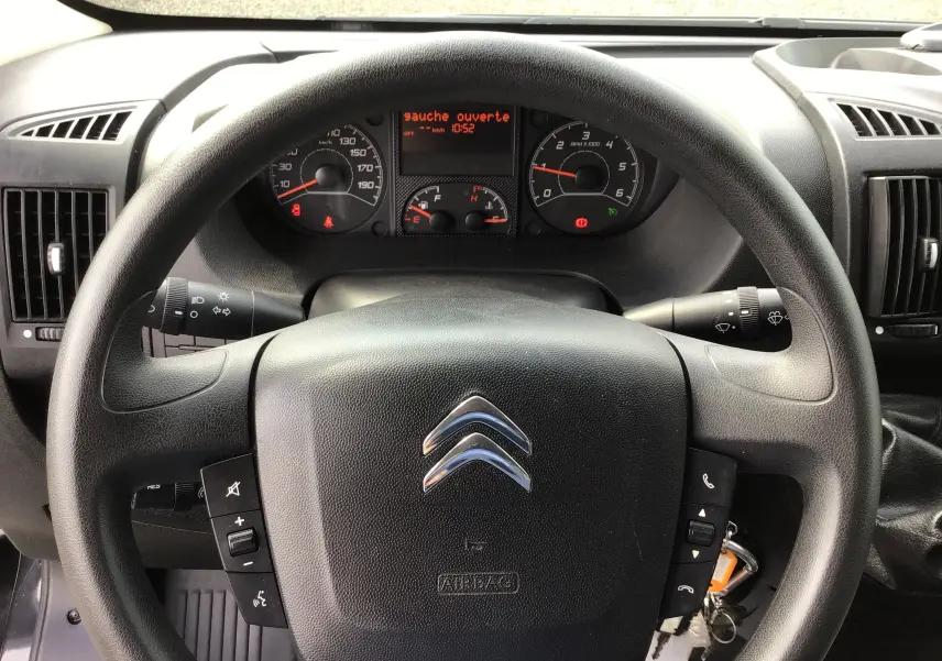 Vue intérieure du tableau de bord et volant du Citroën Jumper gris graphite, avec commandes au volant visibles.