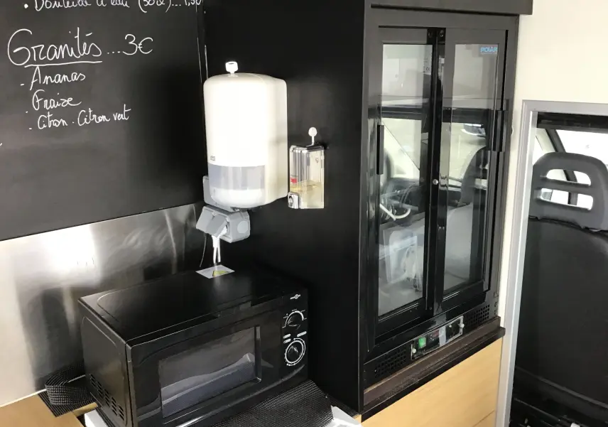 Intérieur du food truck Citroën Jumper gris, vue sur micro-ondes et vitrine réfrigérée côté conducteur.