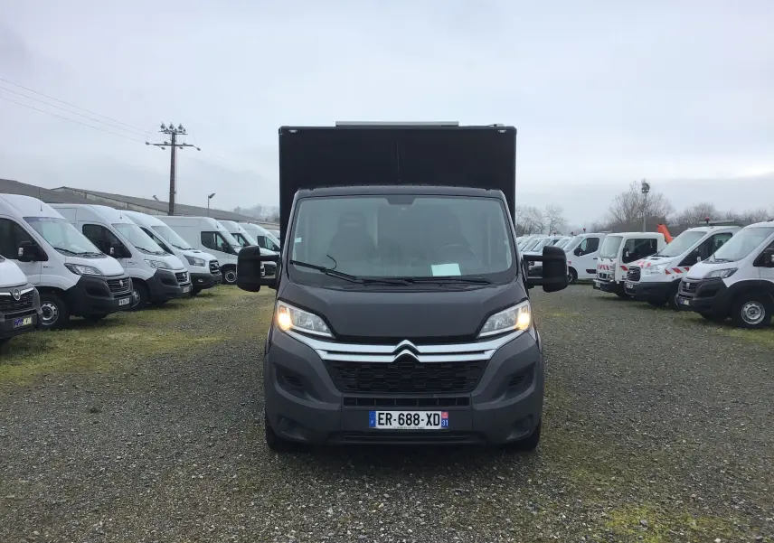 Vue frontale d'un Citroën Jumper plancher cabine gris graphito avec caisse magasin noire et feux allumés.