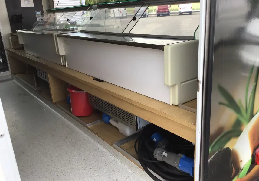 Intérieur du food truck Citroën Jumper gris, vue latérale montrant le plan de travail en bois avec vitrines réfrigérées et rangements.