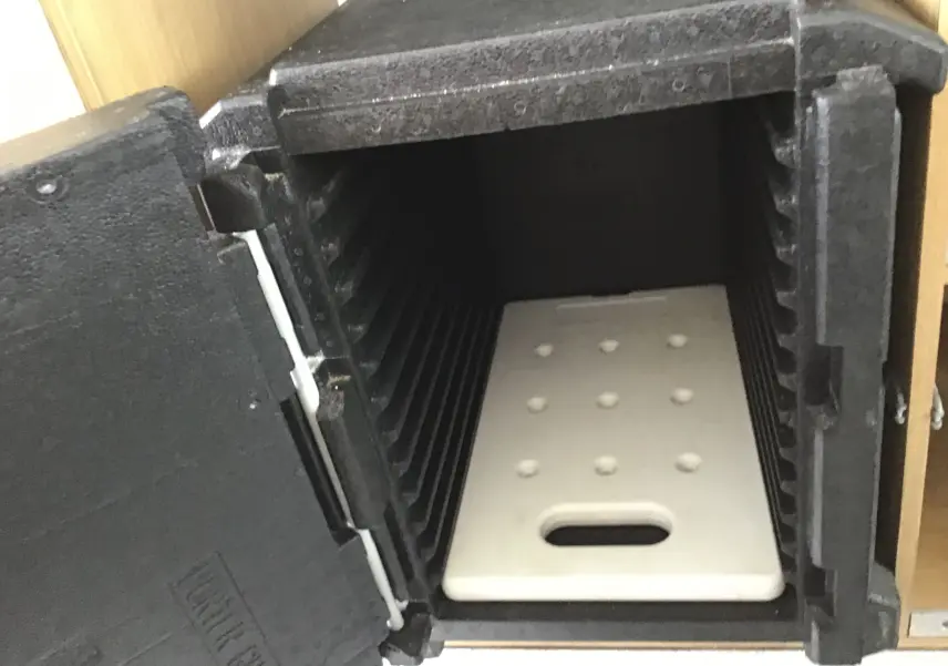 Gros plan sur l'intérieur noir d'une caisse isotherme ouverte avec un plateau blanc perforé visible.