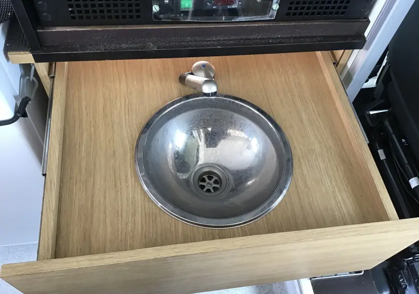 Gros plan sur évier encastré dans tiroir en bois clair à l'intérieur du Citroën Jumper gris Graphito food truck.