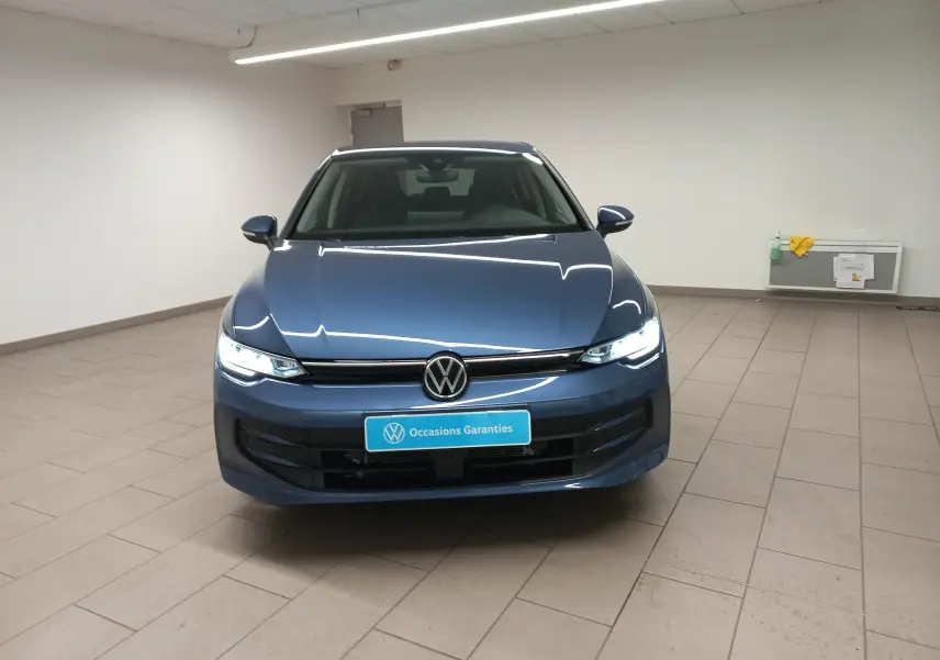 Vue avant d'une Volkswagen Golf 1.5 TSI Bleu Anemone avec phares allumés et plaque "Occasions Garantis" dans un showroom.