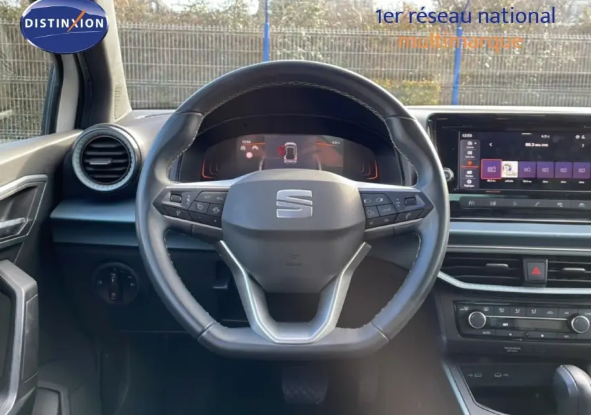 Vue intérieure centrée sur le volant cuir du SEAT Arona 2025 avec tableau de bord numérique et écran tactile.