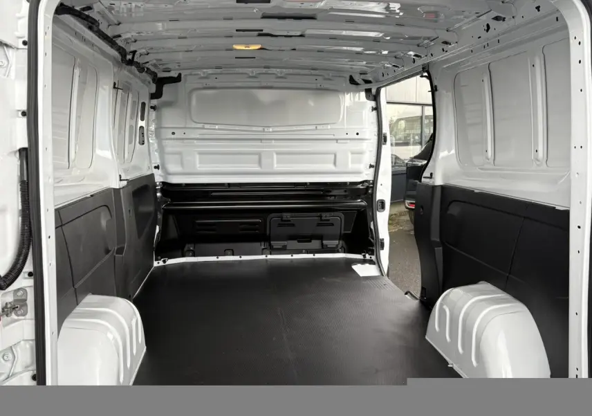 Vue intérieure arrière du Renault Trafic Fourgon blanc Glacier, montrant l'espace de chargement avec plancher bois noir et parois blanches.