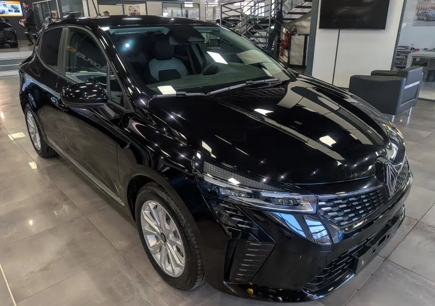 Vue 3/4 avant droite d'une Renault Clio V noire 2025 en intérieur, avec calandre et phares LED distinctifs.