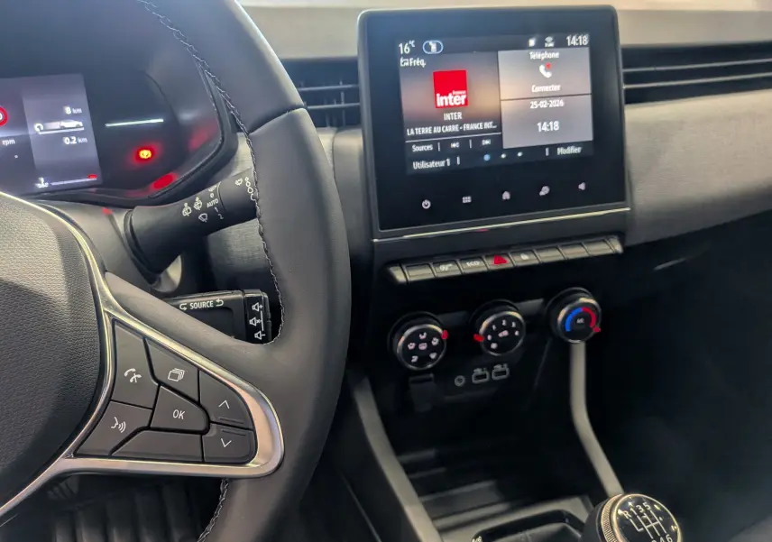 Vue intérieure centrée sur le volant et la console centrale d'une Renault Clio V noire, avec écran tactile et boîte manuelle.