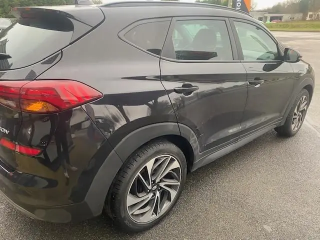 Vue 3/4 arrière droite d'un Hyundai Tucson noir 2019 avec jantes alliage bi-ton et feux arrière allumés.