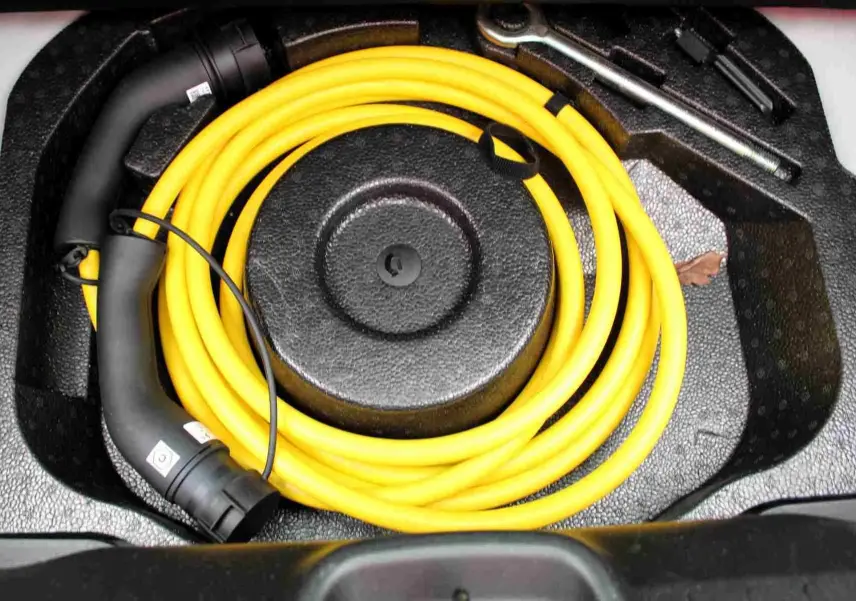 Gros plan sur le câble de recharge jaune enroulé dans le coffre d'une Fiat 500 électrique blanche, avec outils de bord visibles.