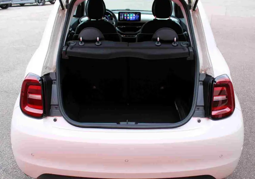 Vue arrière ouverte de la Fiat 500 électrique blanche 2023, coffre vide et tableau de bord avec écran tactile visible.