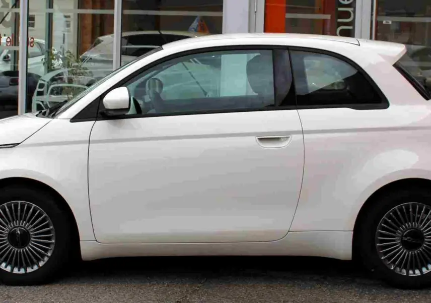 Profil côté gauche de la Fiat 500 électrique blanche 2023, avec jantes spécifiques et lignes arrondies distinctives.