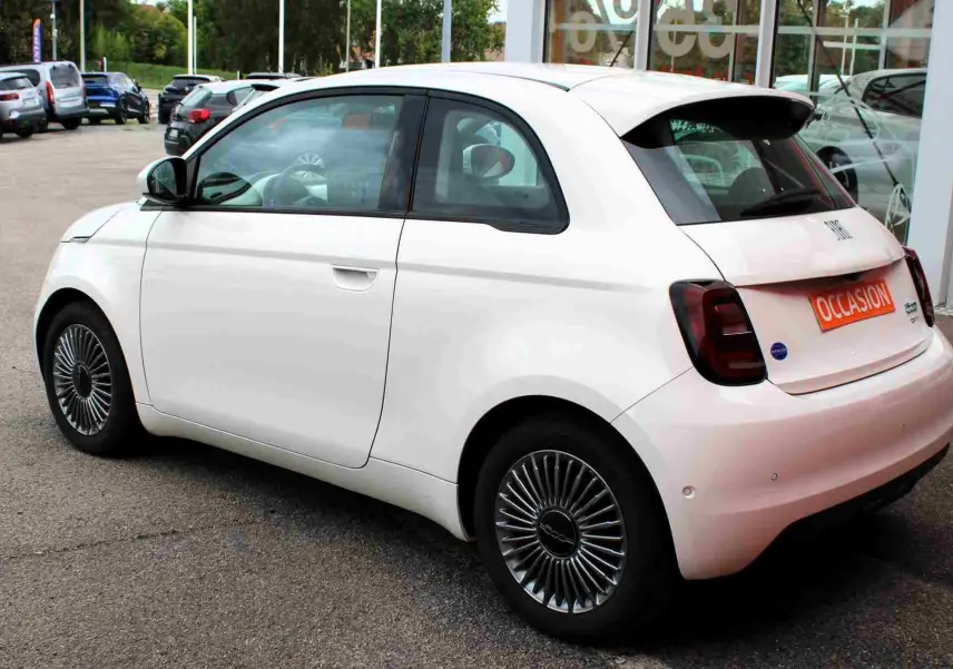 Vue 3/4 arrière droite d'une Fiat 500 électrique blanche avec jantes spécifiques et plaque "OCCASION" visible.