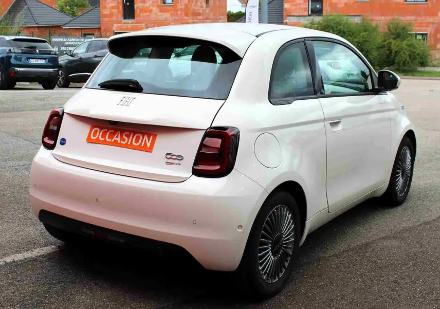 Vue 3/4 arrière droite d'une FIAT 500 électrique blanche de 2023 avec jantes spécifiques et feux arrière foncés.