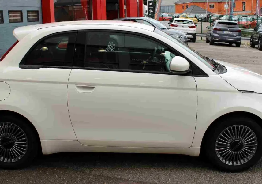 Profil côté gauche de la Fiat 500 électrique blanche 2023, avec jantes spécifiques et rétroviseurs assortis.