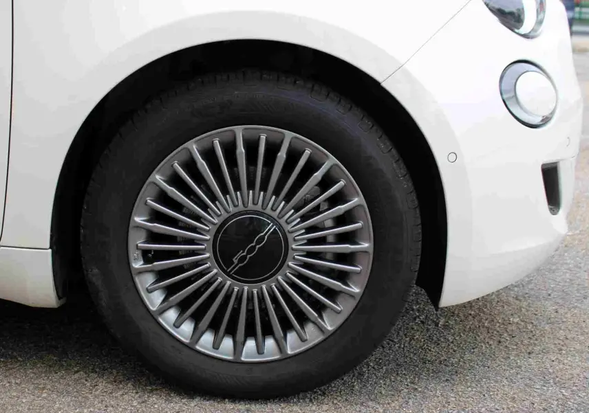 Gros plan sur la roue avant gauche de la FIAT 500 électrique blanche, avec jante au design rayonné argenté.